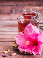 Glass Cup with red tea pink hibiscus flower on dark wood background