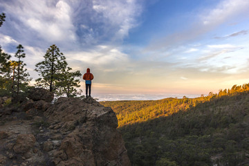 Obraz premium man standing on rock at sunrise with forest below