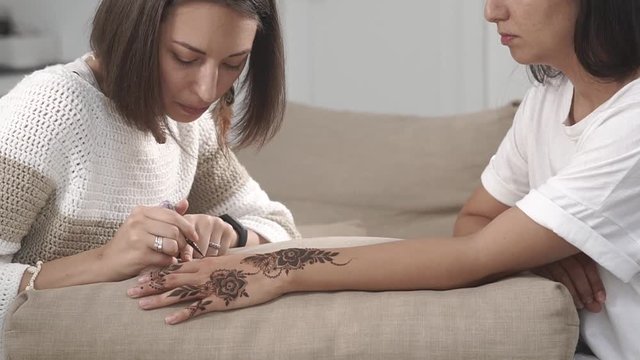 the make-up artist applies the paint to the skin of the hands of the spa visitor, she draws the mehendi, the lady likes to observe the creative process