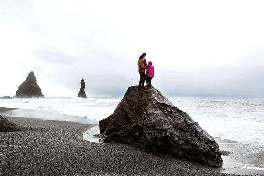 couple of tourists standing on a rock on a black beach in Iceland