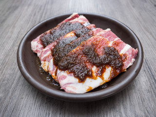 Slice raw pork with marinate in ceramic plate on wood background