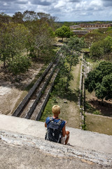 Girl sitting on the steps of the pyramid and looking at the ancient city of Maya Uxmal. Mexico
