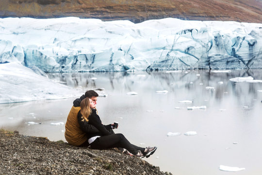 two tourists are sitting near the glacier iceberg in Iceland