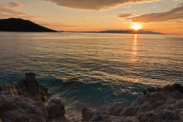 Sun is setting behind Skiathos island with some sea rocks in foreground at Kastani Mamma Mia beach, island of Skopelos, Greece