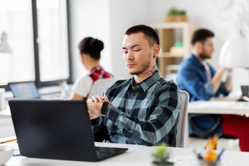 business and technology concept - man with laptop computer and smart watch working at office