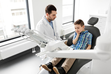 medicine, dentistry and healthcare concept - male dentist with kid patient suffering from toothache at dental clinic adjusting chair