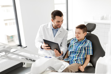 Fototapeta na wymiar medicine, dentistry and healthcare concept - smiling male dentist showing tablet pc computer to kid patient at dental clinic