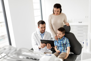 medicine, dentistry and healthcare concept - dentist showing tablet pc computer to kid patient and his mother at dental clinic