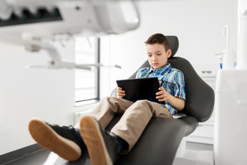 medicine, dentistry and technology concept - happy kid patient with tablet pc computer at dental clinic