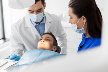 medicine, dentistry and healthcare concept - dentist with mouth mirror checking for kid patient teeth at dental clinic