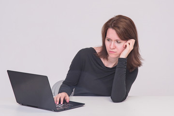 Portrait of beautiful brunette manager girl on white background sitting at table behind laptop