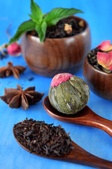 Blossom, black and green sorts of tea in wooden cups and spoons and two anise stars against the blue background