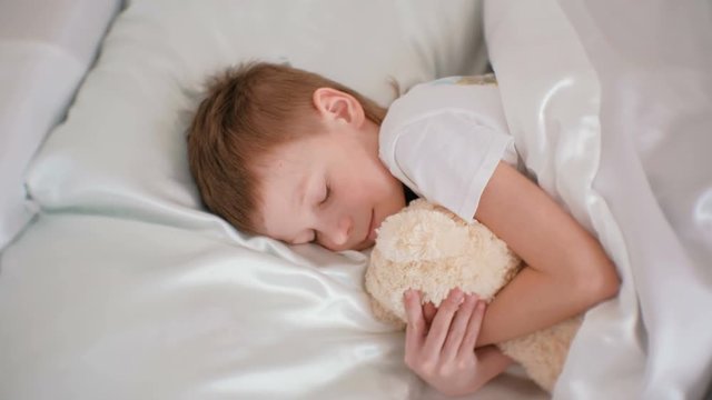 Seven-year-old boy falling asleep hugging toy bear.