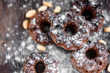 Chocolate cupcakes with sugar powder and peanuts on dark wooden background.