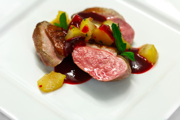 duck breast with pear and cherry sauce with mint on white plate
