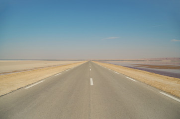 Road on a crest of the constructed dam. Large salt lake Chott el Djerid. Largest salt pan of the Sahara Desert. Below sea level. Nature and travel. Tunisia