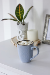 Blue mug with cocoa, coffee, marshmallows on white table with decor