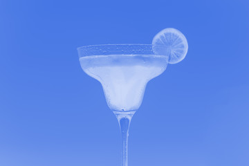 A glass with a white cocktail and lemon on a blue background. Tinted