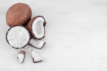 Halves of coconut with coconut shavings and small pieces of coconut on a white wooden background....