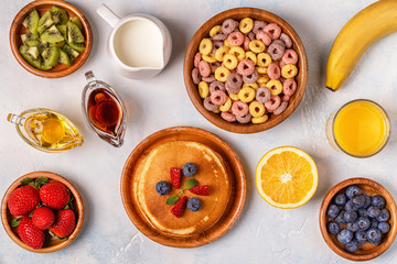 Breakfast with colorful cereal rings, pancakes, fruit, milk, juice.