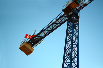 Construction crane with the Turkish flag on top on the cloudless sky, view from the bottom up