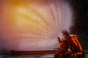 firefighter with a protective helmet uses a foaming agent to extinguish and water from hose for fire fighting, Firefighter spraying high pressure water to fire with copy space.