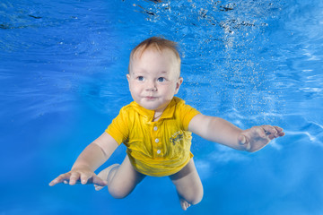Fototapeta na wymiar little boy in a yellow shirt learns to swim underwater in the pool