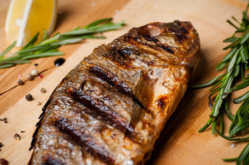 Donand fish baked in a grill. On a wooden board with lemon and rosemary