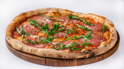 Italian pizza with ham, parma, arugula, parmesan, mozzarella lies on a wooden round board, on a white background