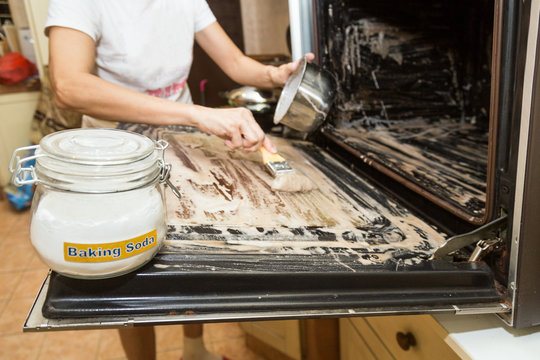 Person Applying Mixed Baking Soda Onto Surface Of Oven