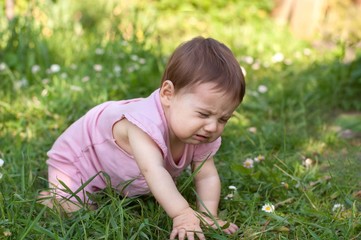 Baby is sitting on grass and crying.