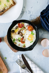 Breakfast of scrambled eggs with tomatoes and greens in a frying pan on the table