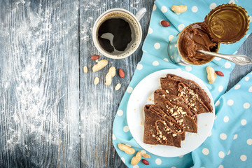 Chocolate oat pancakes with caramel and nuts with cup of coffee on blue fabric and grey wooden table.