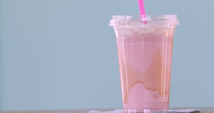 Strawberry milkshake covered with whipped cream in plastic glass isolated on turquoise background