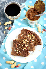 Chocolate oat pancakes with caramel and nuts with cup of coffee on blue fabric and grey wooden table.