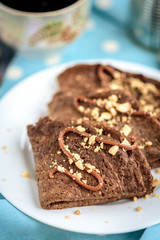 Chocolate oat pancakes with caramel and nuts with cup of coffee on blue fabric and grey wooden table.