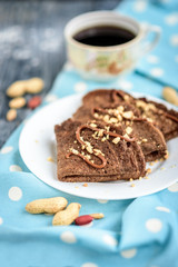 Chocolate oat pancakes with caramel and nuts with cup of coffee on blue fabric and grey wooden table.