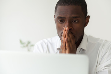 Thoughtful hopeful African American employee looking at computer laptop screen, waiting hoping,...