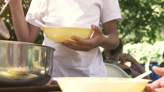 Young Happy Kids Preparing Eating Lunch Pasta In Summer Camp Outside On Sunny Day In Park Serving Food From Pot Pan Slow Motion