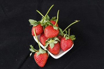 very fresh strawberries in white plate on a black background,

