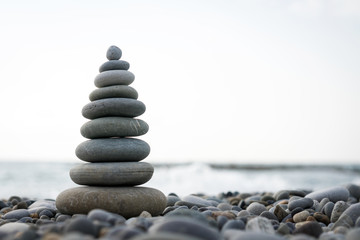 a pyramid of stones on a pebble beach against the sea and sky.