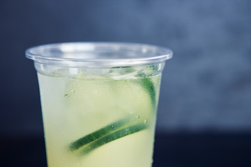 Cold cucumber lemonade in the plastic cup on the black background