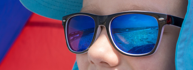 Ausschnitt eines Kindergesichtes mit in der Sonnenbrille spiegelnden Strand
