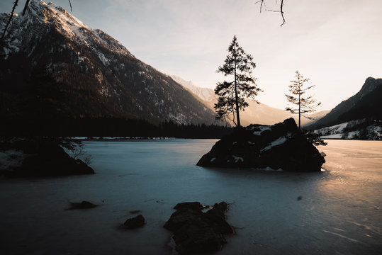 Sonnenuntergang in den bayrischen Alpen am See in den Bergen am Hintersee mit Blick auf eine kleine Insel auf der zwei B&auml;ume stehen und Bergen im Hintergrund