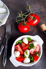 Caprese salad with mozzarella, tomato, basil and balsamic vinegar arranged on white bowl on stone background
