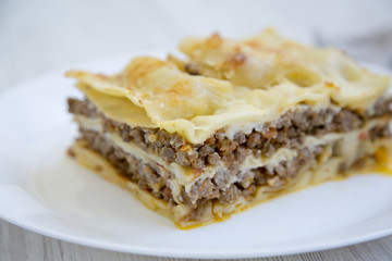 Italian beef lasagne on a white round plate, white wooden background. Side view.