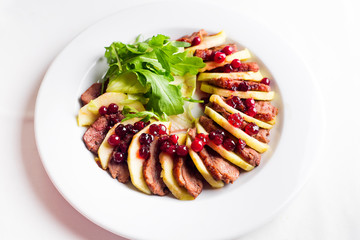 Salad with slices of duck breast with apples and salad under cowberry sauce
