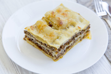 Delicious beef lasagne served on a white round plate, white wooden background. Side view.