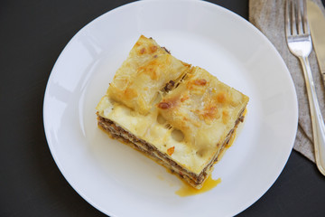 Traditional beef lasagne on a white round plate, dark background, top view.