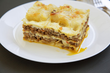Traditional meat lasagne on a white round plate on dark table. Side view. Close-up.